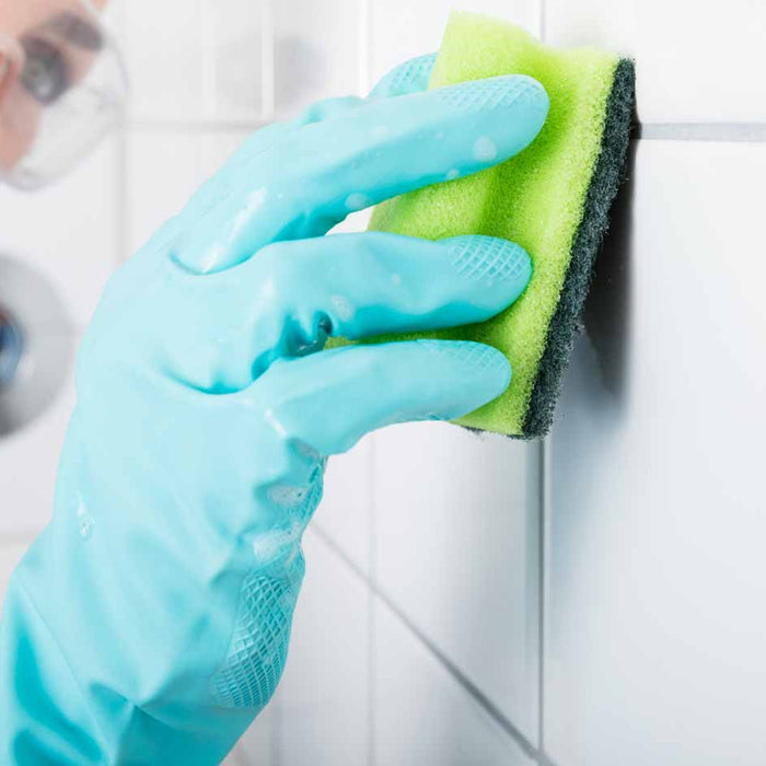 cleaning a white wall tile with a sponge and rubber gloves