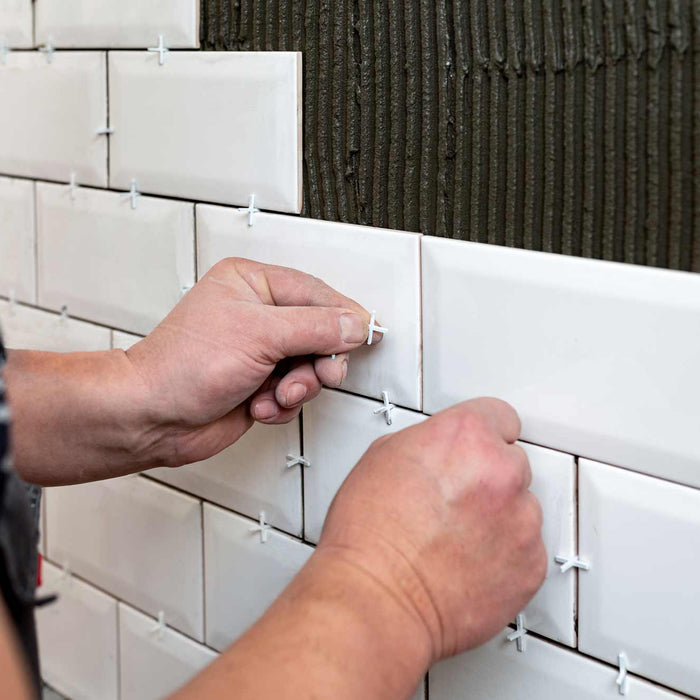 person applying tile spacers to metro white tiles that have been fixed to a wall with trowelled adhesive 
