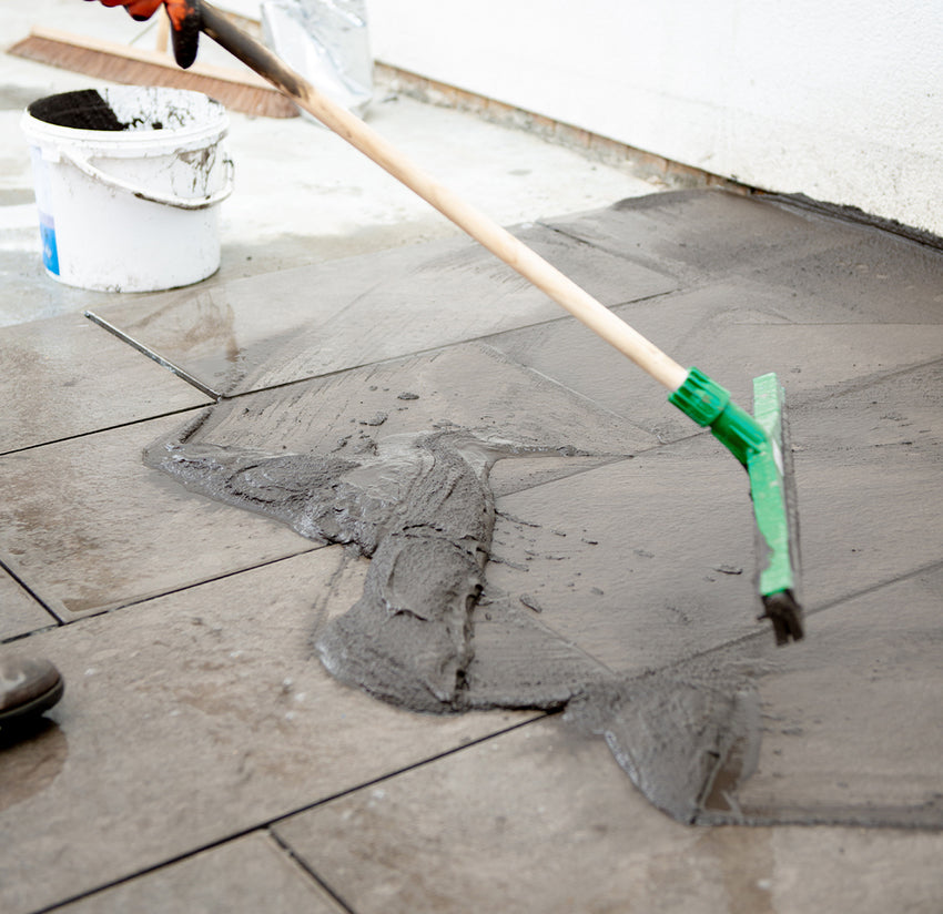 squeegee moving mortar grout over outdoor tiles