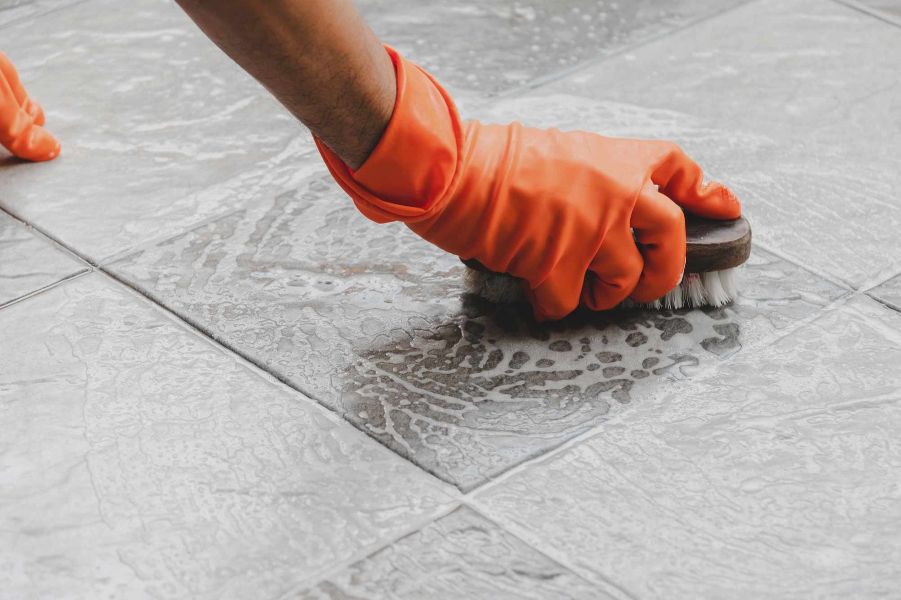 rubber gloves and brush with cleaning solution cleaning outdoor tiles.
