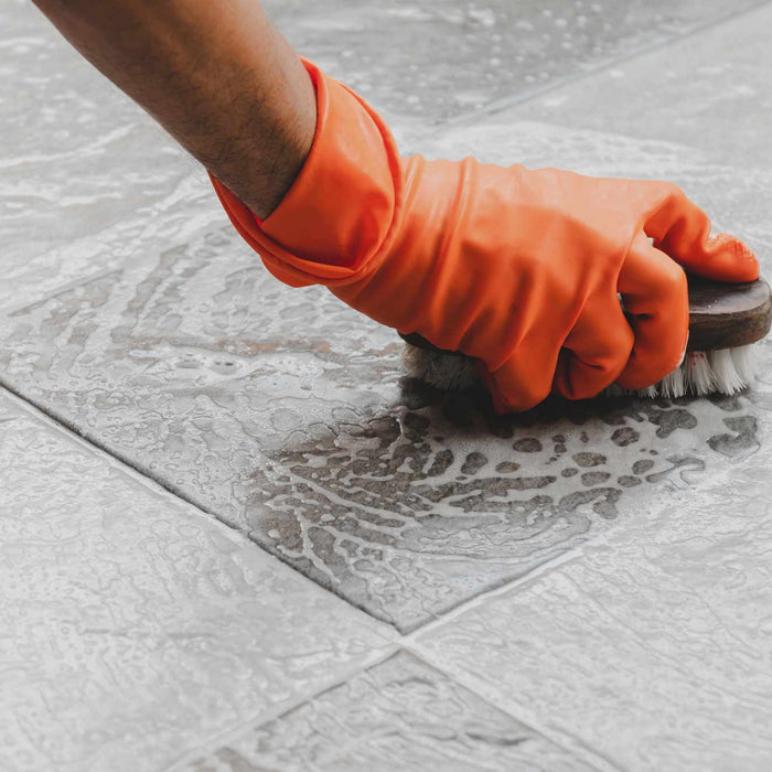 rubber gloves and brush with cleaning solution cleaning outdoor tiles.