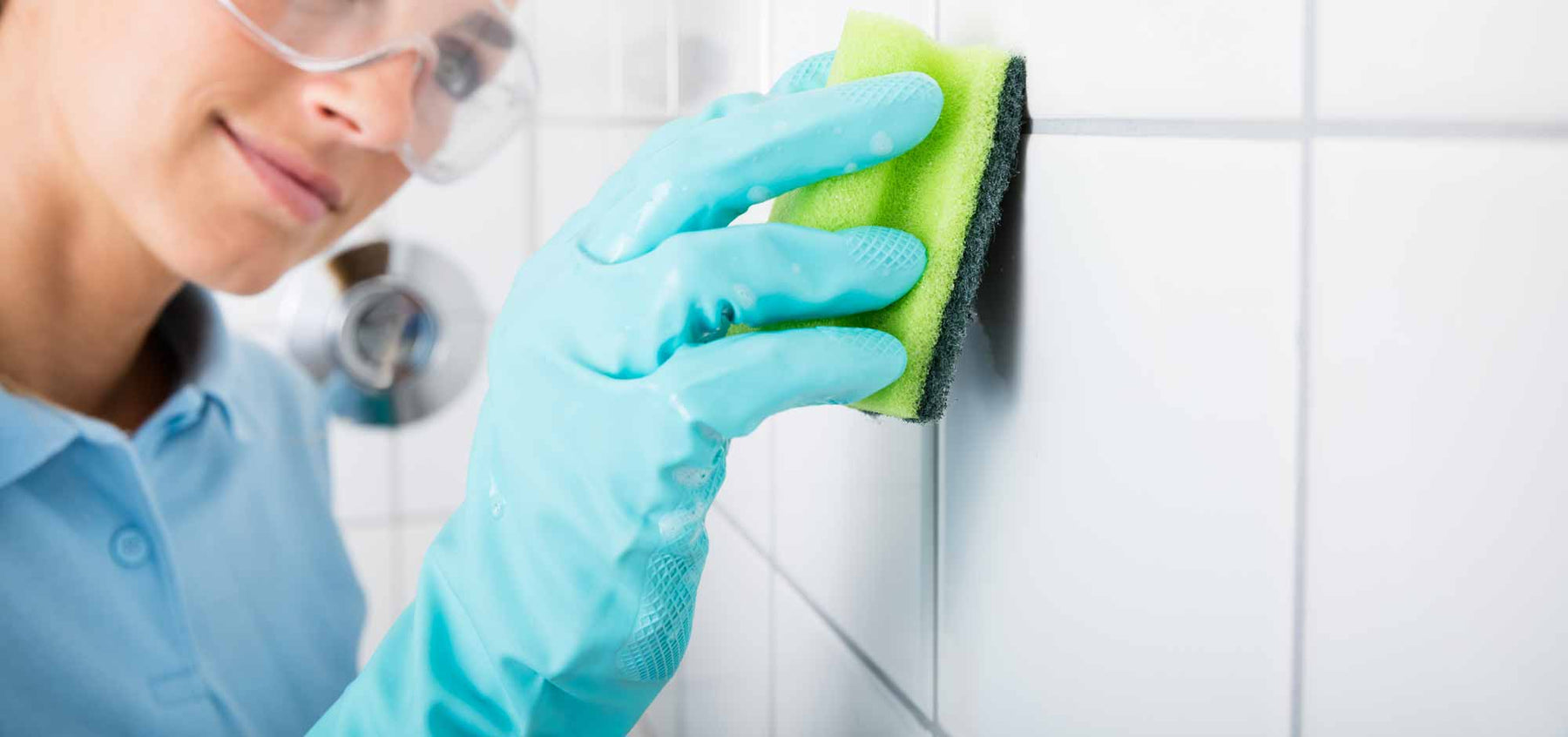 cleaning a white wall tile with a sponge and rubber gloves