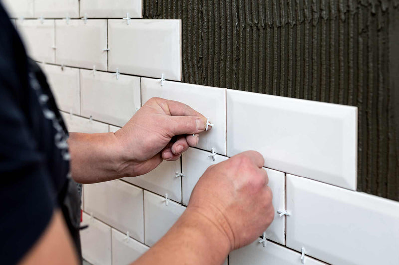 Image of person applying tile spacers to metro white tiles that have been fixed to a wall with trowelled adhesive 
