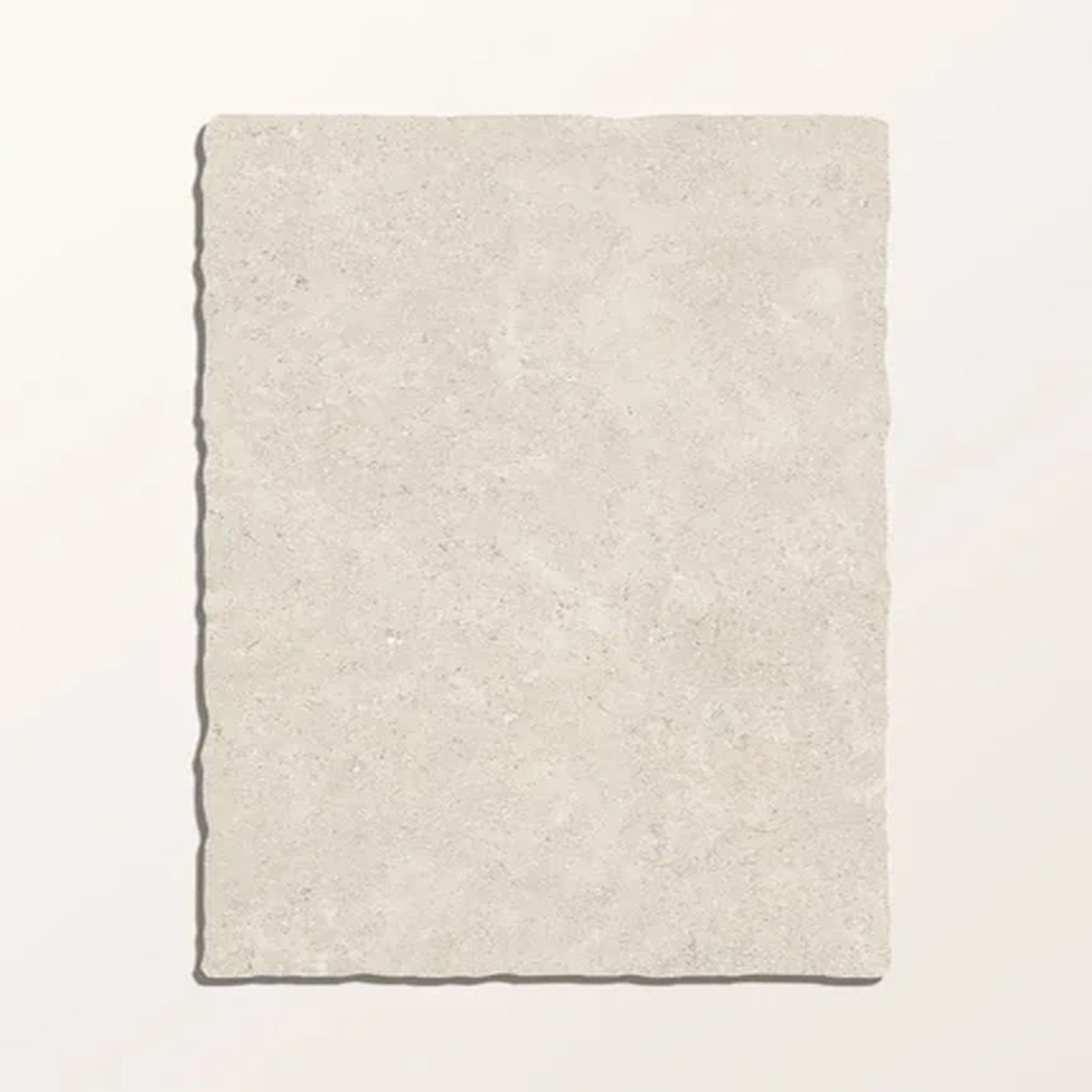 Image of A rectangular stone tile with rough, uneven edges in a light beige colour, displayed flat against a solid off-white background.