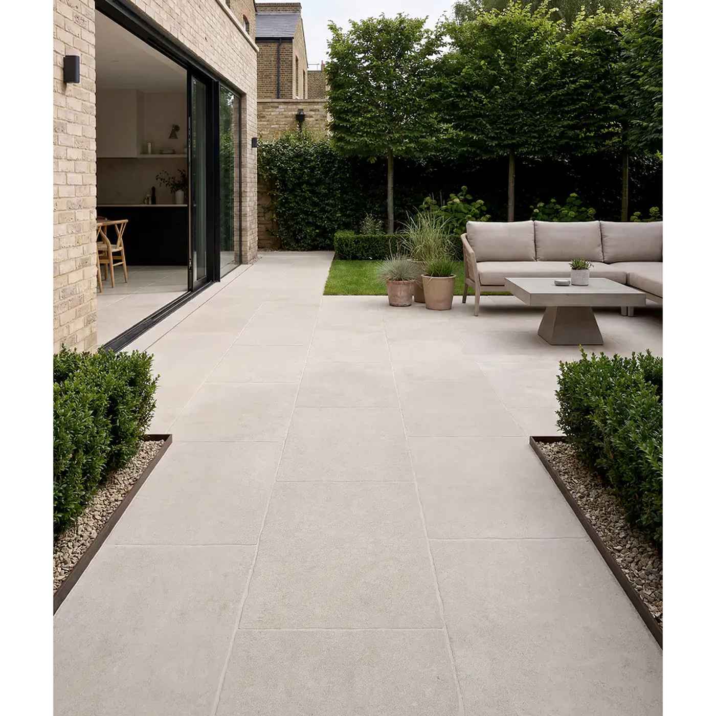 Image of Wychwood Claire porcelain paving in a contemporary garden patio setting, featuring soft light beige stone-effect slabs, sleek outdoor lounge furniture, landscaped planting, and seamless indoor-outdoor living