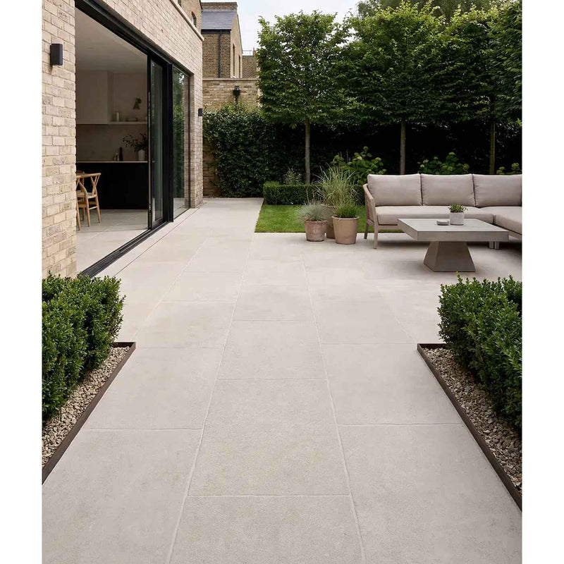 Image of Wychwood Claire porcelain paving in a contemporary garden patio setting, featuring soft light beige stone-effect slabs, sleek outdoor lounge furniture, landscaped planting, and seamless indoor-outdoor living