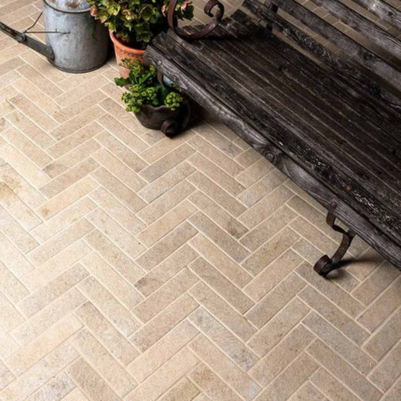 Image of Beige rectangular stone tiles arranged in a herringbone pattern on a porch next to a dark weathered wooden bench and potted plants.