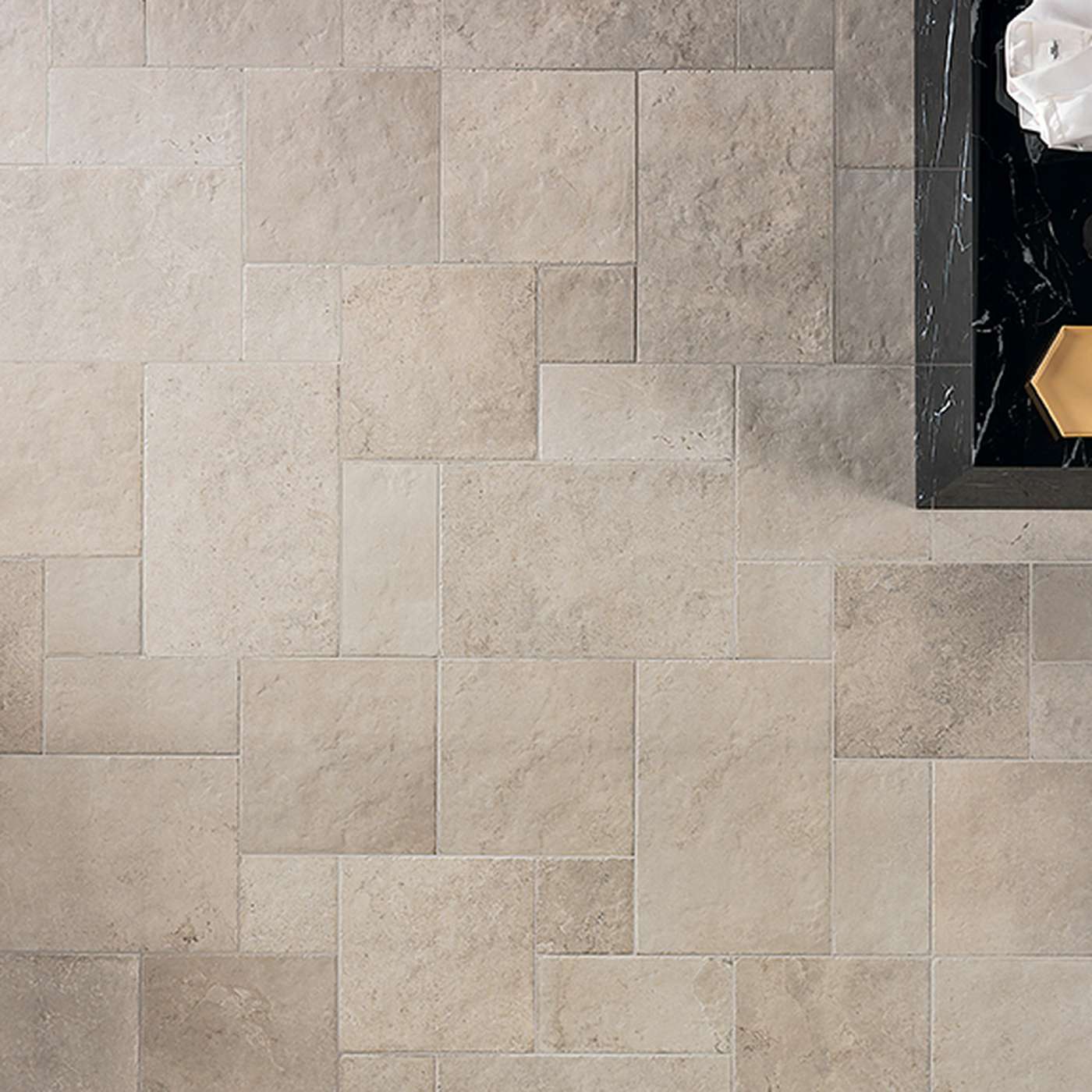 Image of Light grey rectangular stone-look floor tiles arranged in a staggered layout, with a dark marble shelf and decorative objects visible on the right side.