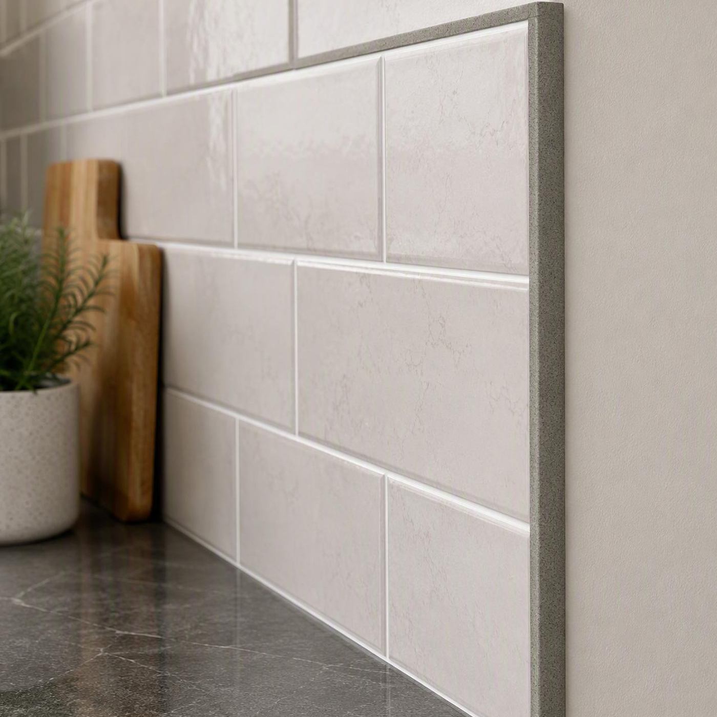 Image of White subway tile backsplash with a grey tile trim and dark grey countertop, styled with wooden cutting boards and a small potted plant.