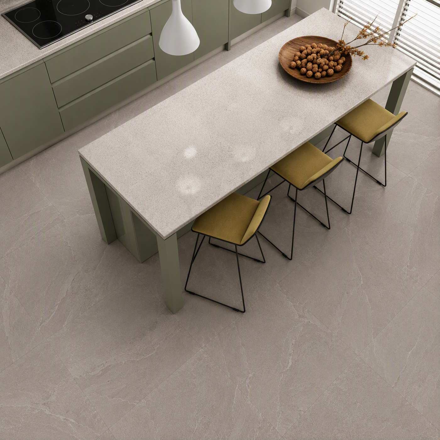 Image of A modern kitchen island with a light stone-look rectangular table and four olive-green chairs, shown from an elevated angle on a matching stone-look floor. The kitchen cabinets are sage green, and a wooden bowl of walnuts sits on the table.