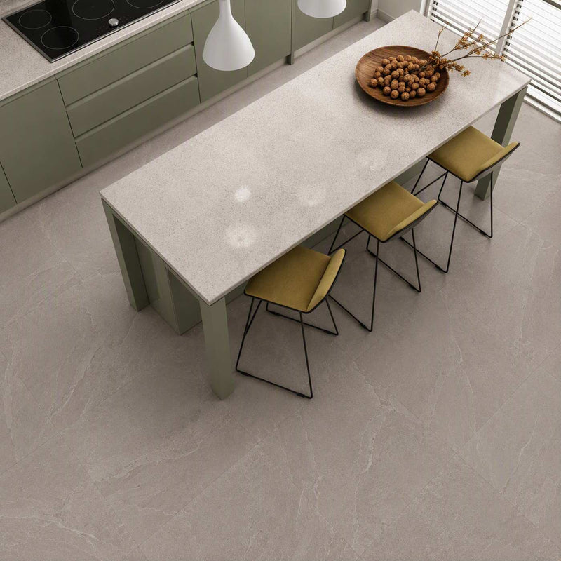 Image of A modern kitchen island with a light stone-look rectangular table and four olive-green chairs, shown from an elevated angle on a matching stone-look floor. The kitchen cabinets are sage green, and a wooden bowl of walnuts sits on the table.