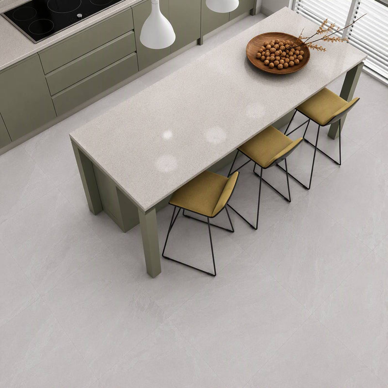Image of A modern kitchen scene with a rectangular light stone dining table, four mustard-yellow upholstered chairs with black metal frames, pendant lights, cabinetry, and a bowl of nuts on the tabletop.