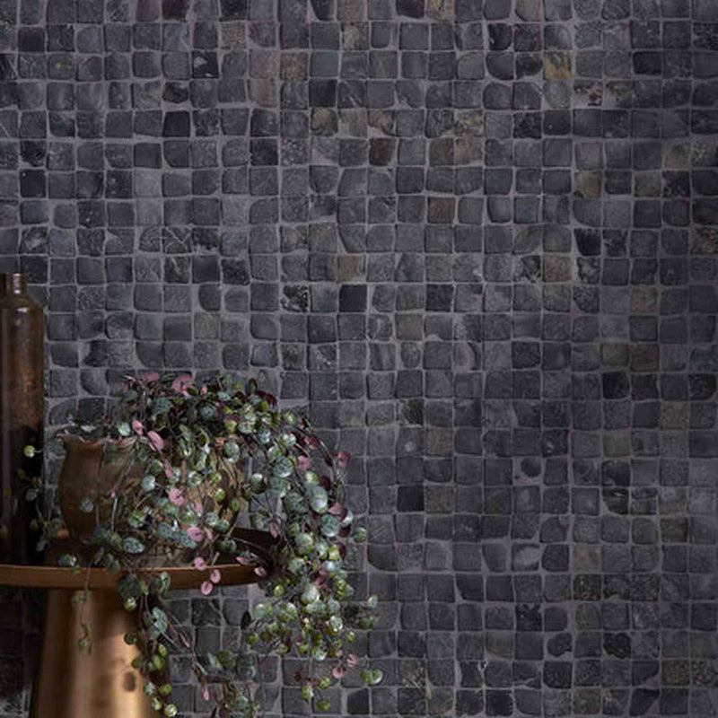 Image of Dark charcoal gray mosaic tile wall with a rustic bronze table and trailing green and pink plant in the foreground.