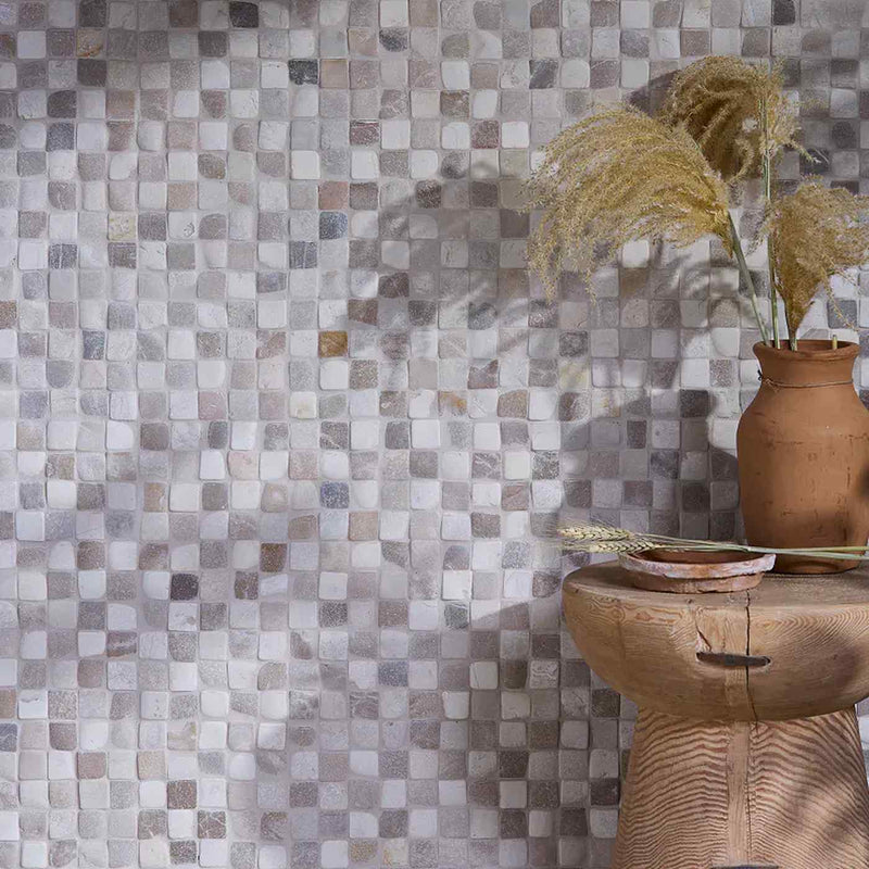Image of Square mosaic tile wall in neutral tones of beige, gray, and brown, styled with a terracotta vase holding dried pampas grass on a rustic wooden pedestal.