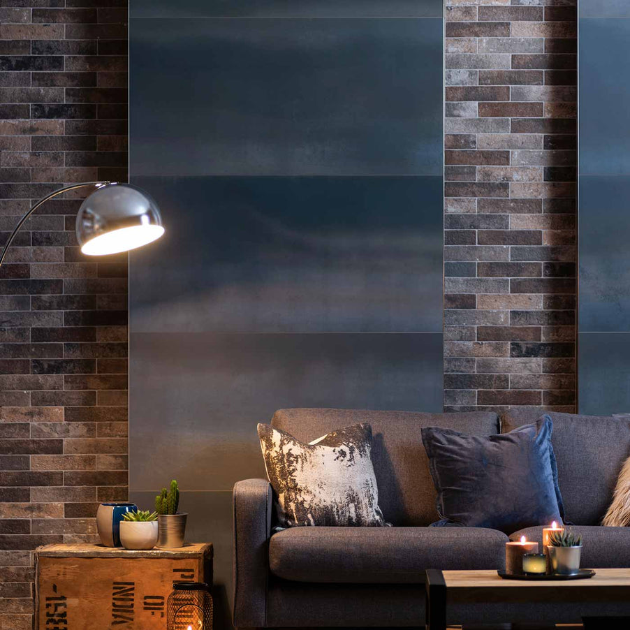 Click to expand Steel Midnight Blue Metallic Finish tile 60x120cm in a lounge setting with brick wallpaper either side. Dark blue sofa with velvet cushions, wooden coffee table and crate side table. Succulent plants sit on top of the tables. Dome floor lamp to the left.