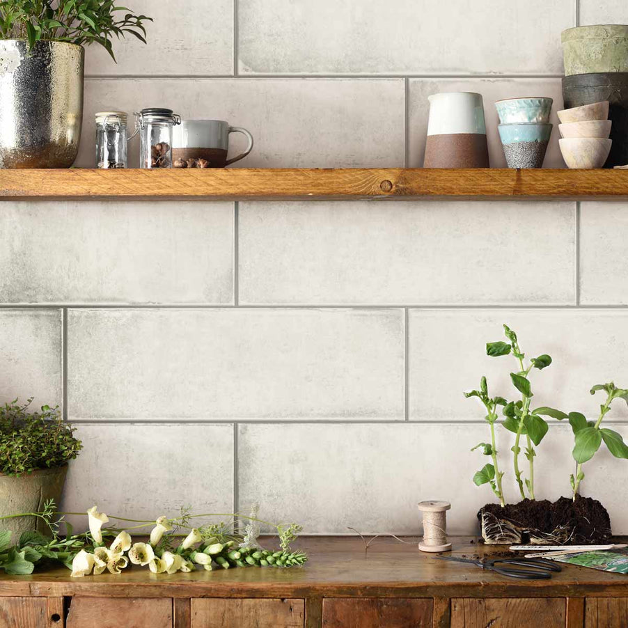 Montblanc White Tile Original Style Tileworks 20x60cm - glossy tiles in a kitchen setting. Tiles on the far wall with wooden kitchen units and shelving attached. Green potted plants sit on the shelves, as well as jugs, scissors and needle and thread.