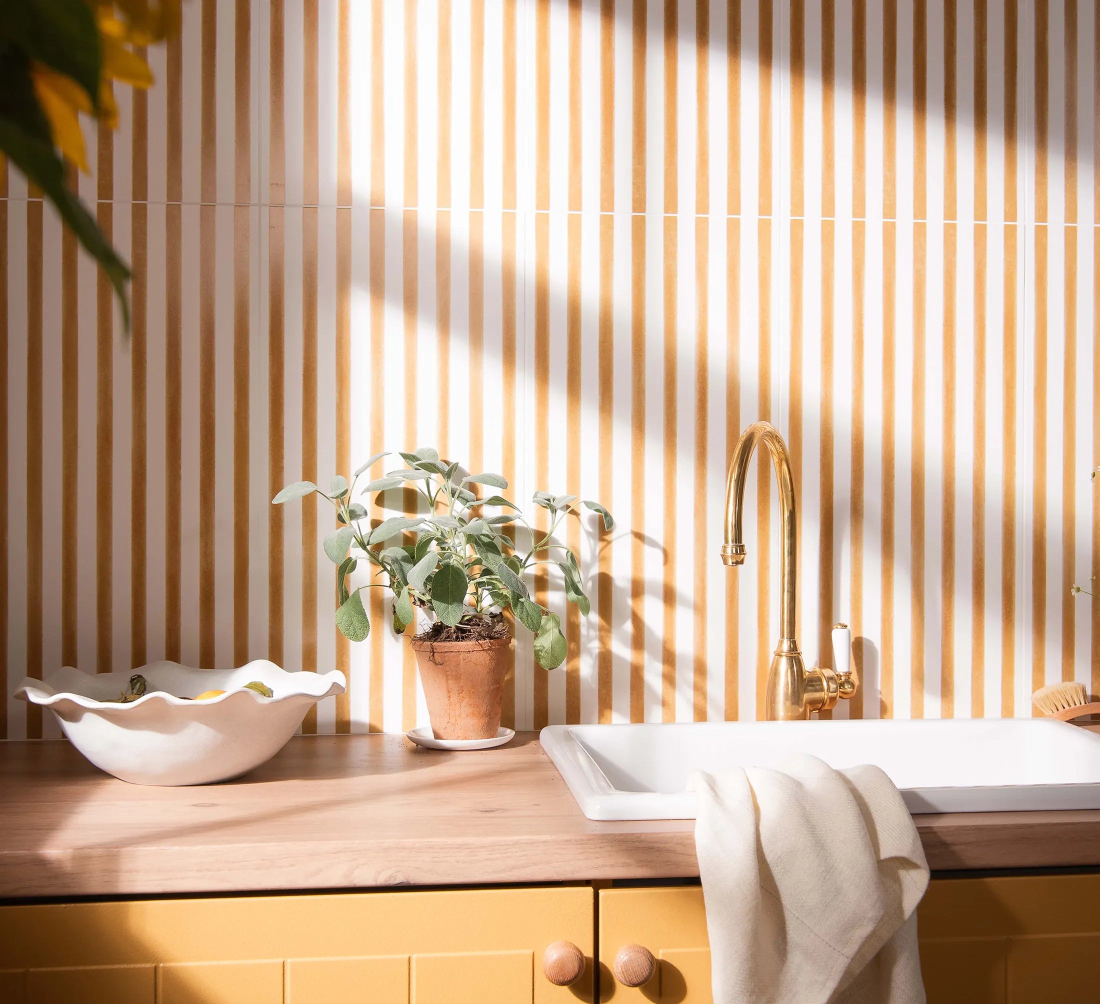 Kitchen counter with a plant, bowl, and gold faucet against yellow striped wall wall tiles.