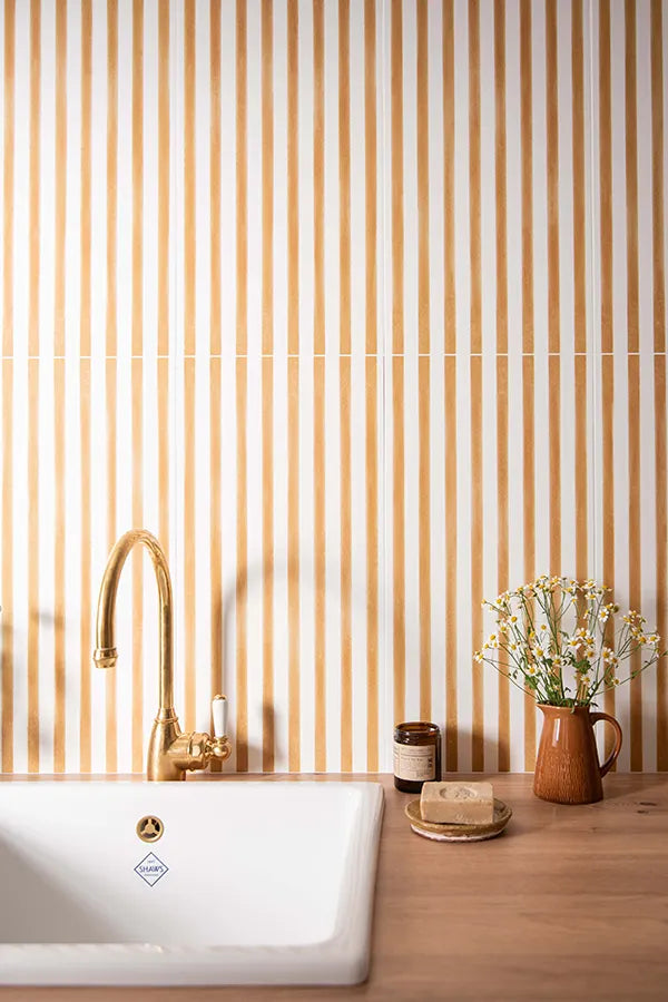 Kitchen counter with a plant, bowl, and gold faucet against yellow striped wall wall tiles.