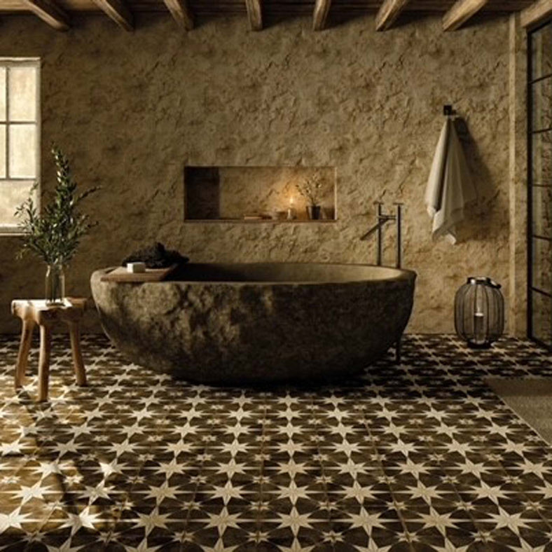 Star Dark Night Pattern Floor Tiles 45x45cm in a bathroom setting. Mud like walls with big mud replica freestanding bath. Wooden stool with glass vase and green flowers. Metal lantern on the floor.