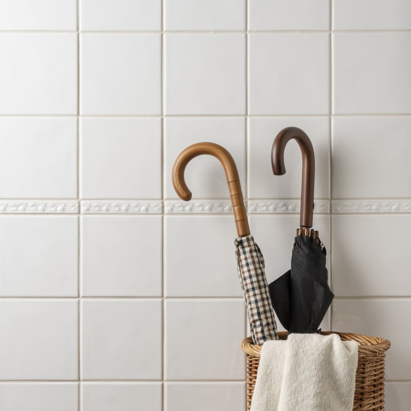 Image of Two umbrellas in a basket against a white tiled wall