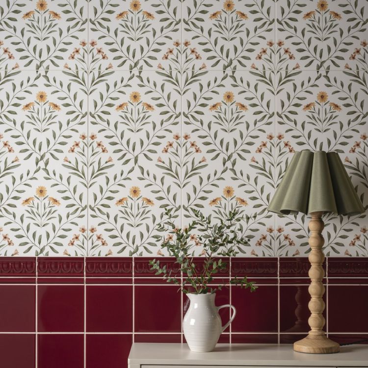 Image of Floral wall tiles with a red border, a jug of greenery, and a wooden lamp.