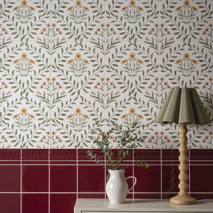 Floral wall tiles with a red border, a jug of greenery, and a wooden lamp.
