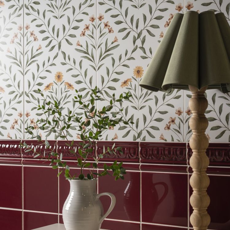 Image of Floral wall tiles with a red border, a white jug of greenery, and a wooden lamp with a green shade.
