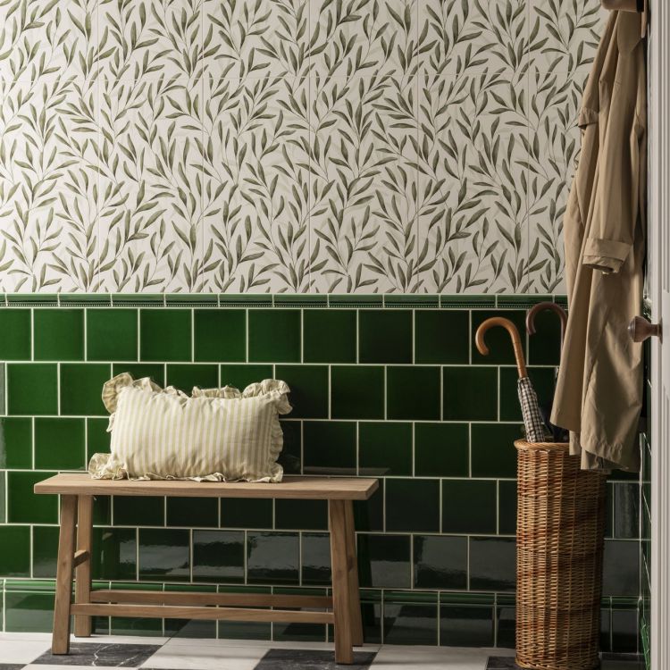 Image of Leaf-patterned wall tiles with a green tiled border, a wooden bench, and a wicker umbrella stand.