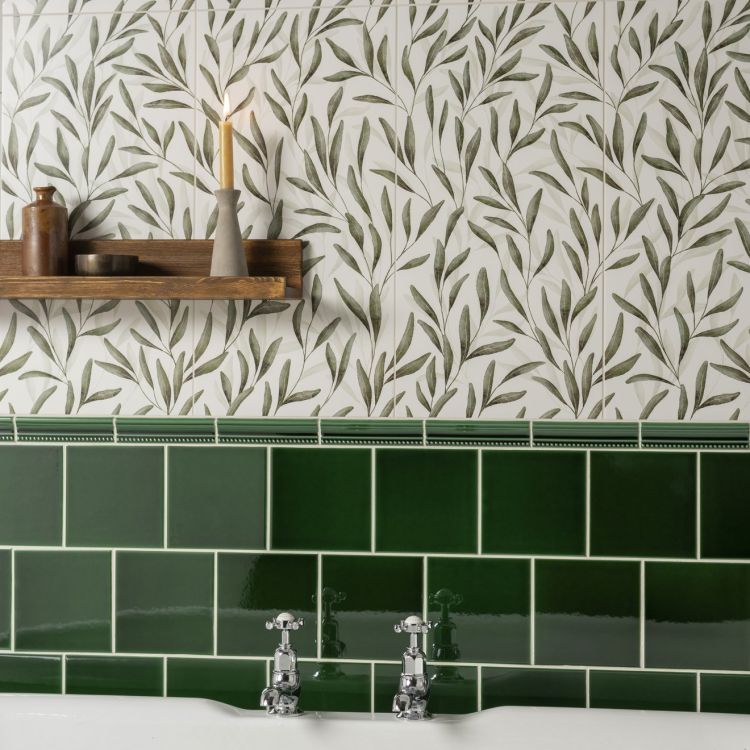 Image of Leaf-patterned wall tiles with a wooden shelf, candle, and green tiled border above a sink.