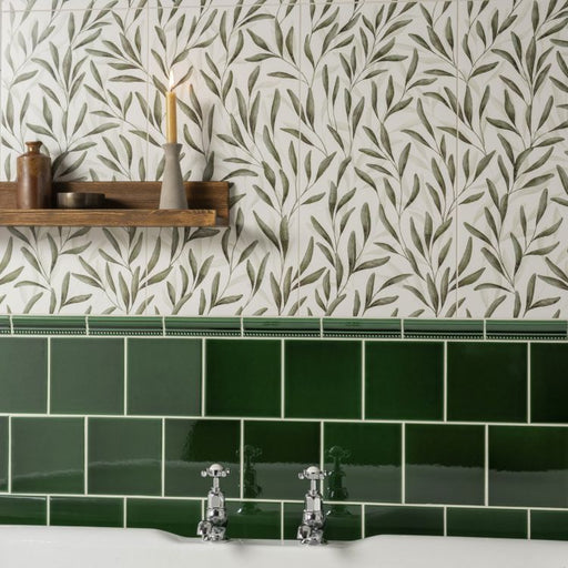 Leaf-patterned wall tiles with a wooden shelf, candle, and green tiled border above a sink.