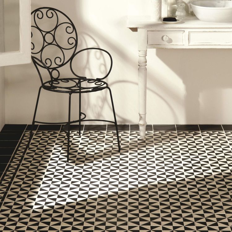 Image of Black metal chair on a black and white patterned floor with a white wall and table in the background.