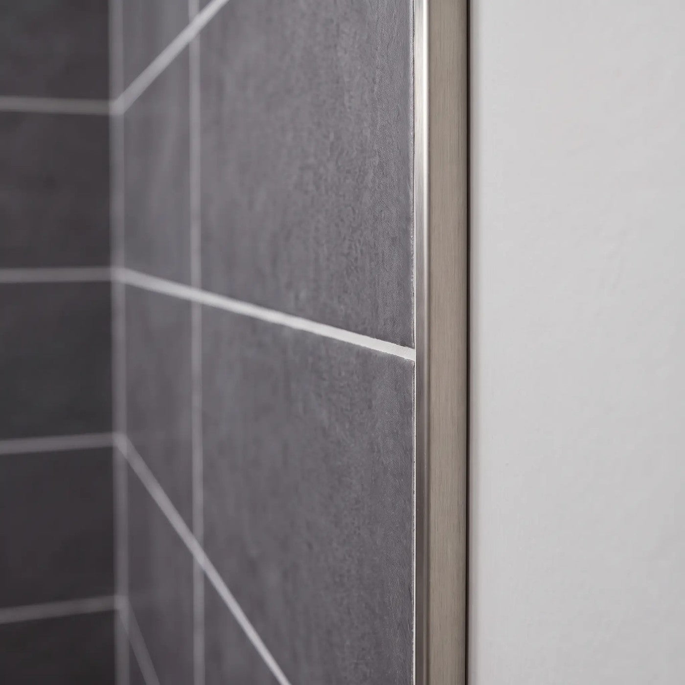 Image of Close-up of a brushed stainless steel tile trim fitted to the edge of dark grey wall tiles in a bathroom.