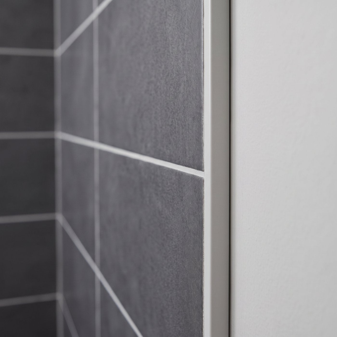 Image of Close-up of a light grey PVC tile trim fitted to the edge of grey ceramic wall tiles in a bathroom, finishing the tile edge cleanly against the wall.