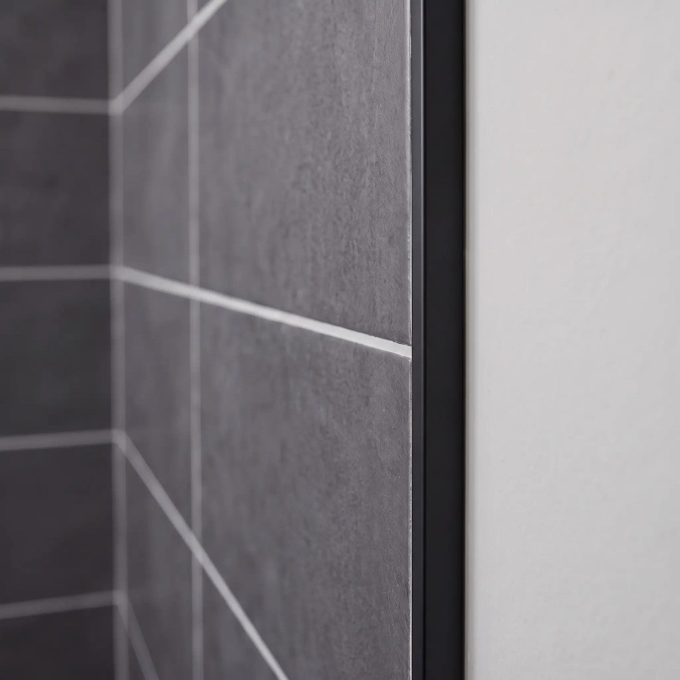 Image of Close-up of a matt black tile trim fitted to the edge of dark grey wall tiles in a bathroom.