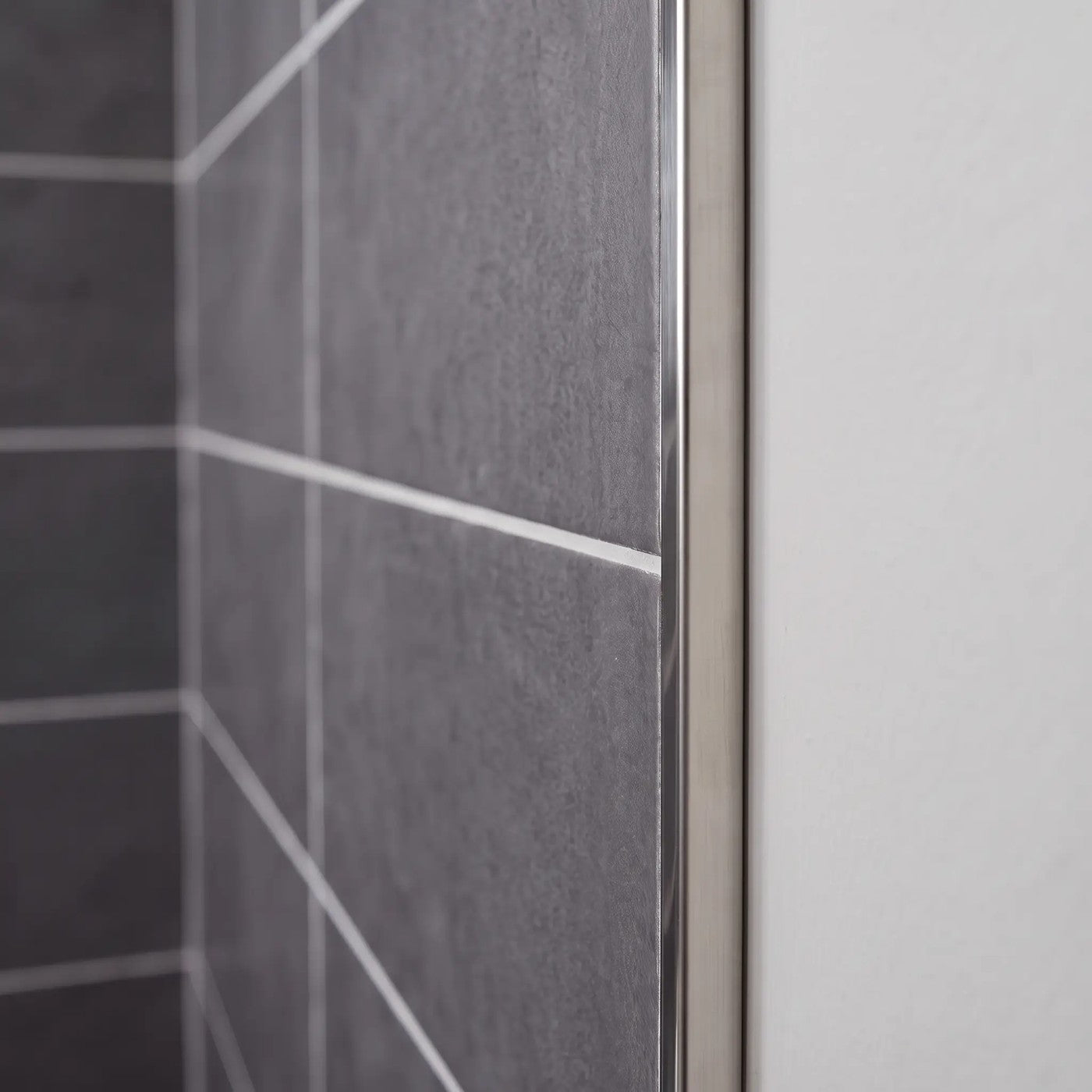Image of Close-up of a polished stainless steel tile trim fitted to the edge of dark grey wall tiles in a bathroom.