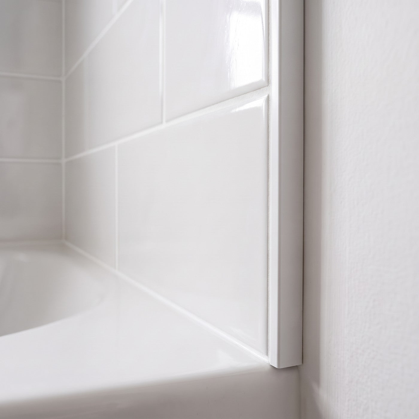 Image of Close-up of a white PVC tile trim fitted to the edge of glossy white ceramic wall tiles above a bath, finishing the tile edge cleanly against the wall.