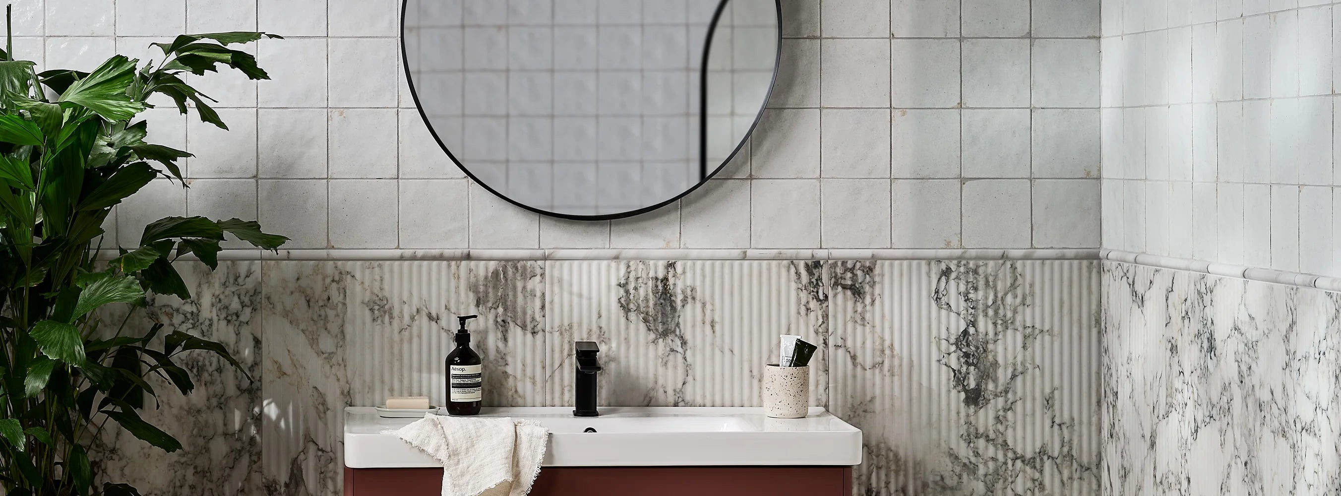 Modern bathroom with a round mirror, sink, and decorative tiles that look like marble.
