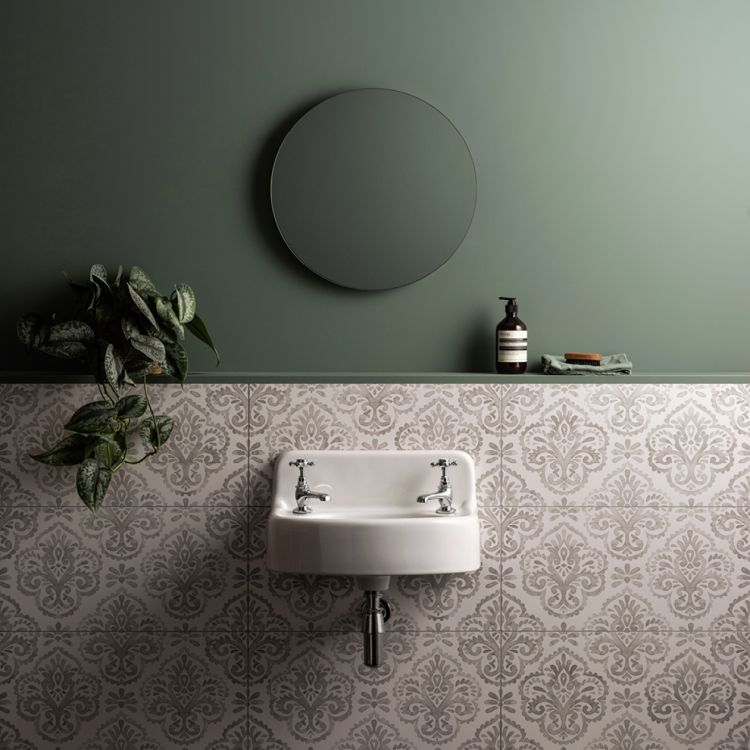 Image of Bathroom with a round mirror, sink, and decorative tiles on a green wall.