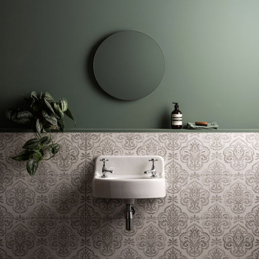 Bathroom with a round mirror, sink, and decorative tiles on a green wall.