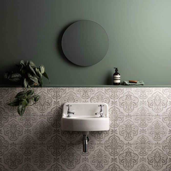Bathroom with a round mirror, sink, and decorative tiles on a green wall.