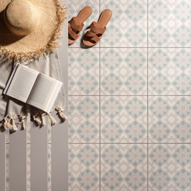 Image of A straw hat, open book, and striped towel lie on patterned floor tiles, with a pair of brown sandals placed nearby.