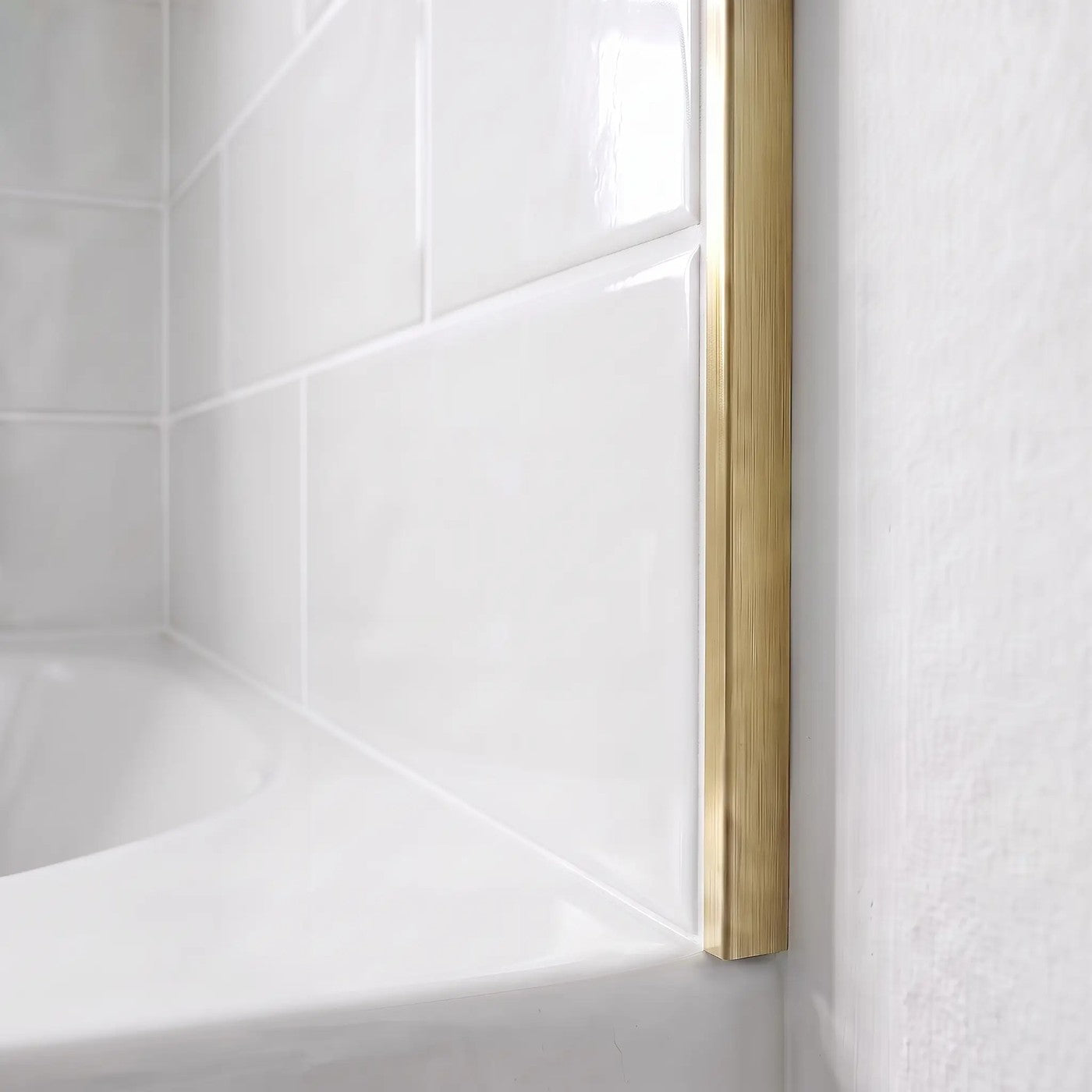 Image of Close-up of a brushed brass straight edge tile trim finishing the edge of glossy white ceramic wall tiles above a bath.