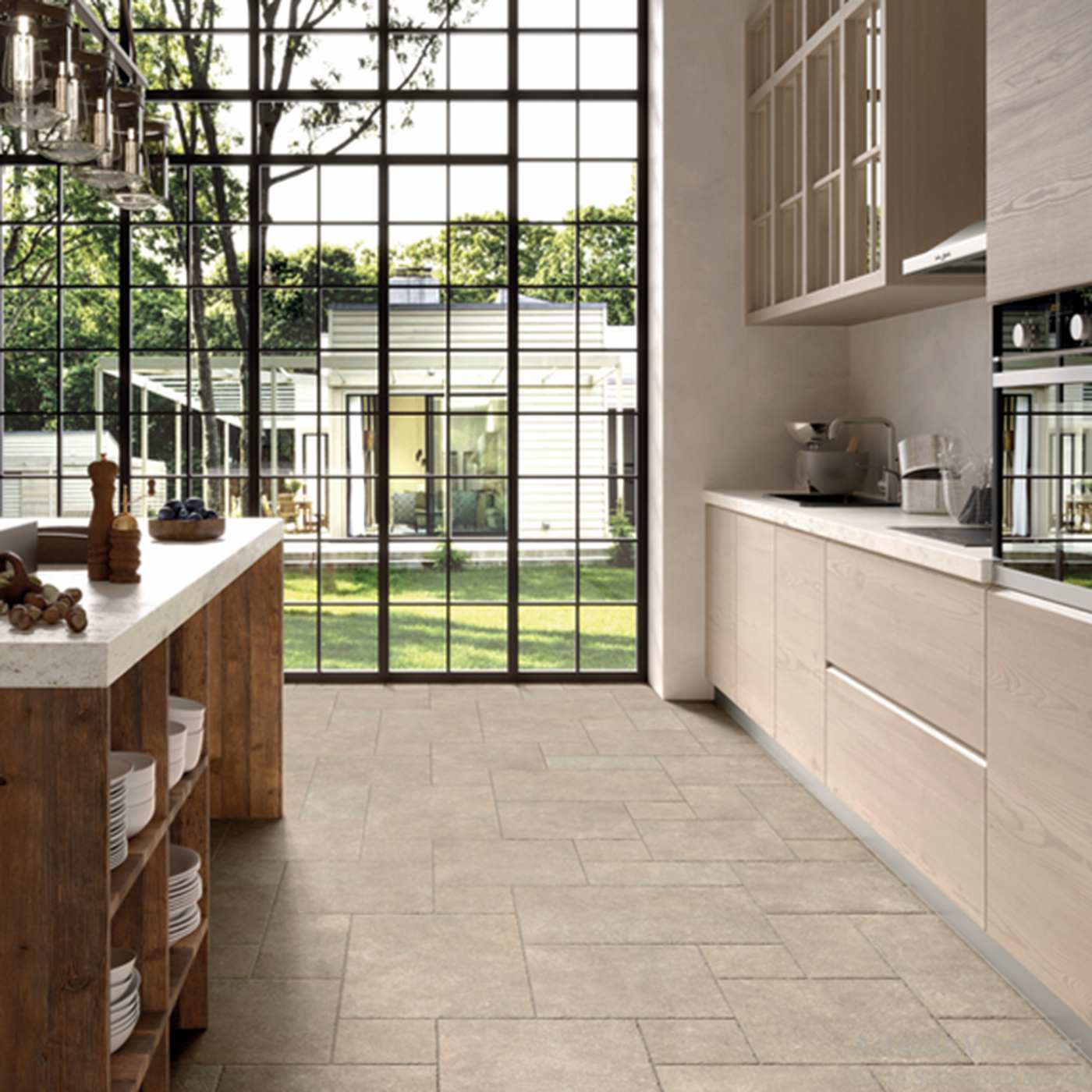 Image of A modern kitchen interior with light beige stone-look floor tiles, light wood cabinetry, a white countertop, and a large black-framed window looking out onto greenery.
