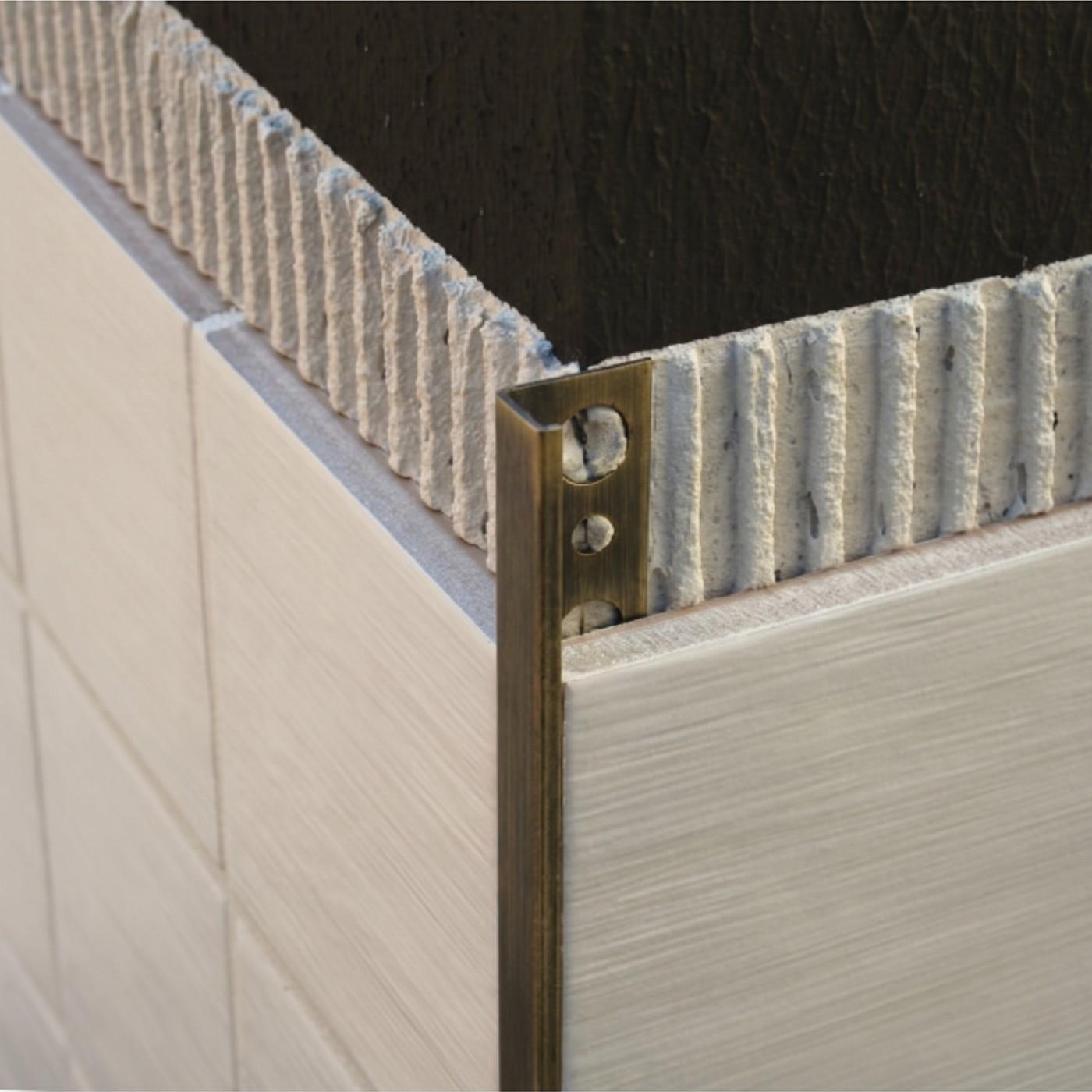 Image of Close-up of an antique brass tile trim fitted to the edge of cream ceramic wall tiles at an external corner