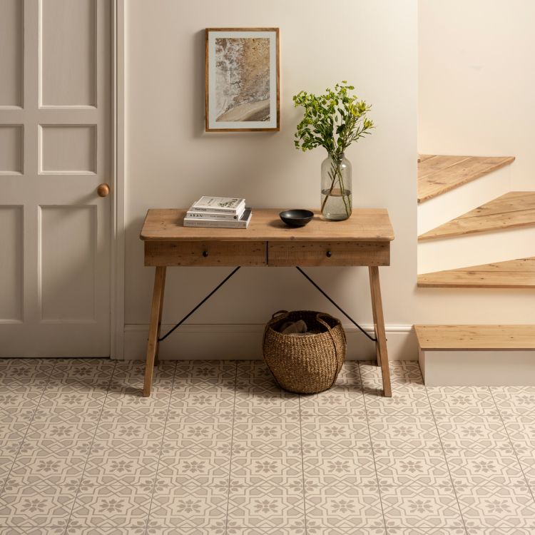 Image of hallway with patterned floor tiles, a wooden console table holding books and a vase of greenery, and wooden floating stairs to the right.