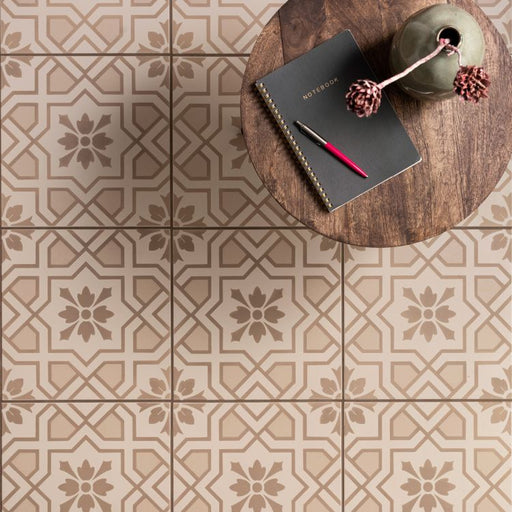 Decorative tiles with geometric pattern on a floor, featuring a notebook and pen on a wooden stool.