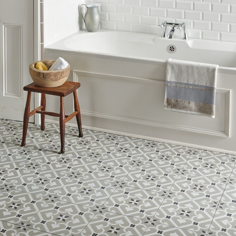 Image of Bathroom with patterned grey and white floor tiles, featuring a freestanding bath, a towel draped over the side, and a small wooden stool with bath accessories