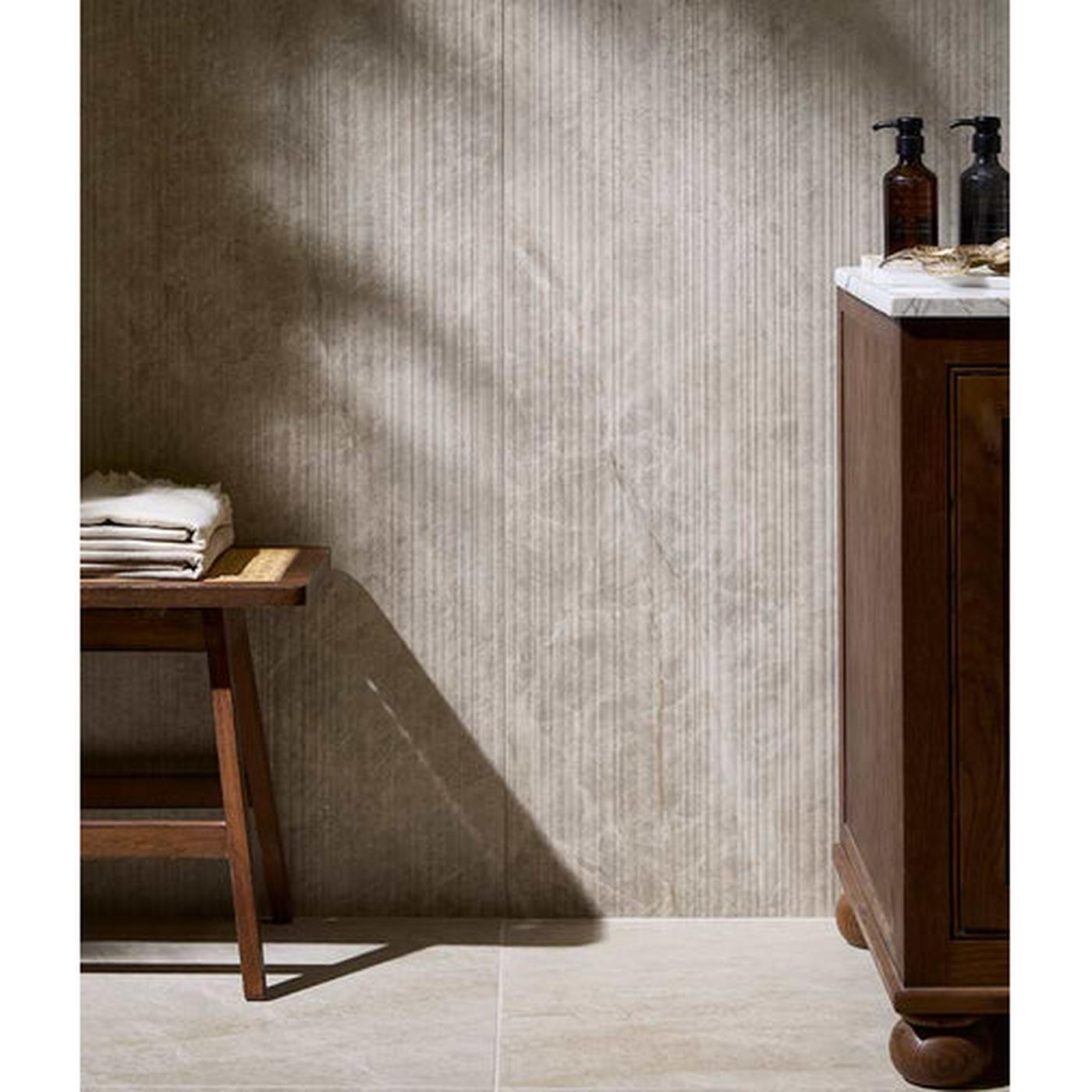 Image of A styled bathroom corner with a textured beige wall, light stone floor, a dark wood vanity with a marble top, a small wooden stool with folded towels, and two dark pump bottles on the counter.