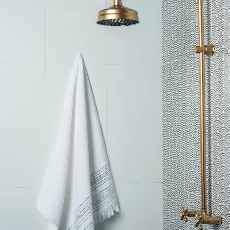 Image of Gold shower fixture next to a wall with a grey scallop pattern, with a white towel hanging on a plain tiled wall.
