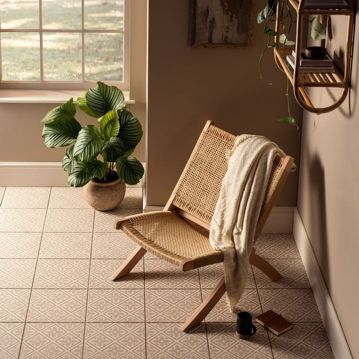 Wicker chair with a towel draped over it in a sunlit room with plants and a window.